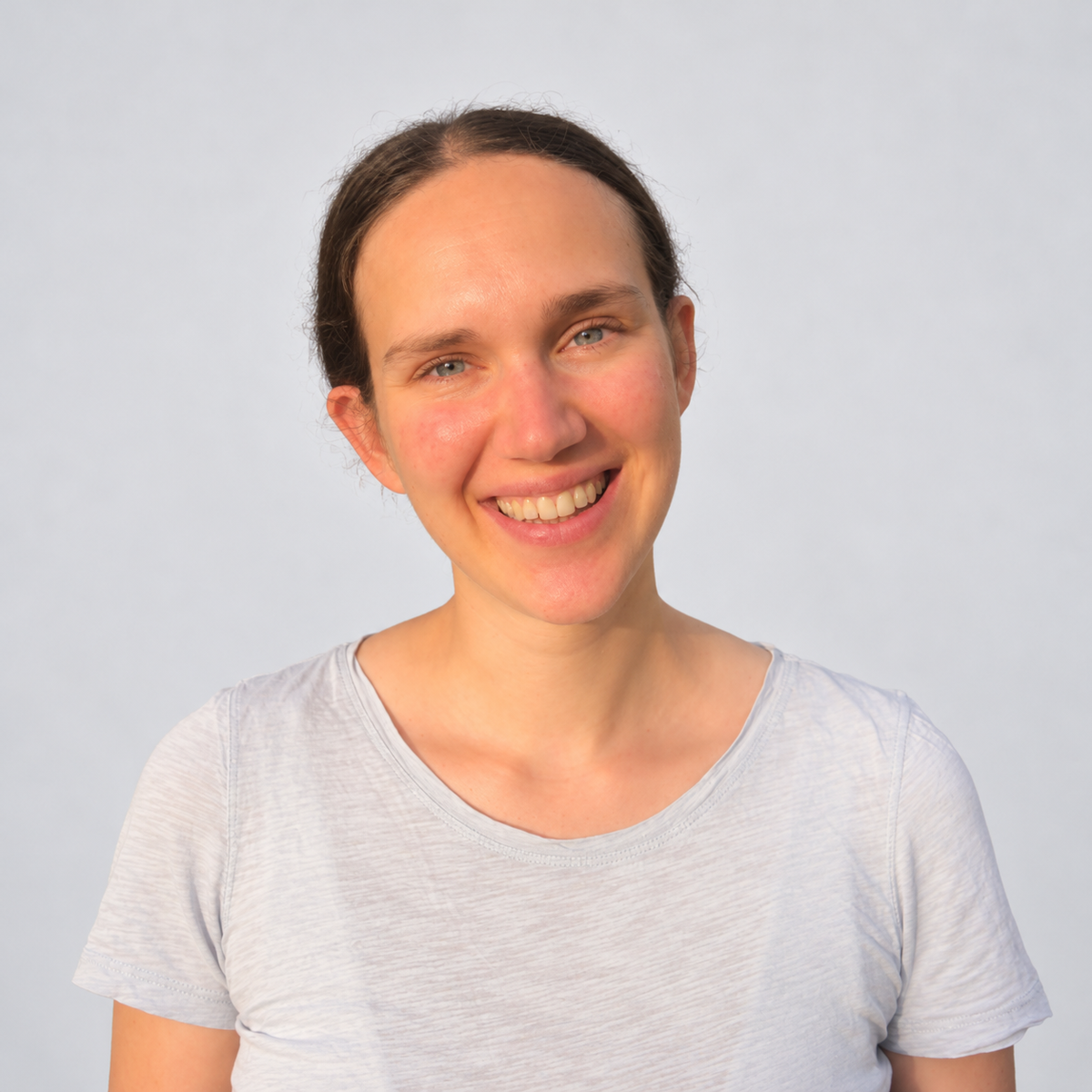 Porträtaufnahme einer Frau im hellen Shirt vor hellem Hintergrund.